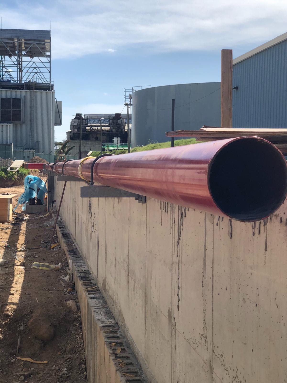 A long red-coated fire-main pipe running toward camera on the BELCO power-station site in Bermuda