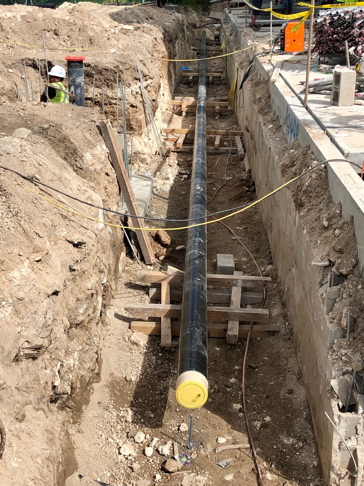 Black-coated fire main bedded on timber bearers down a shored trench, capped at the near end