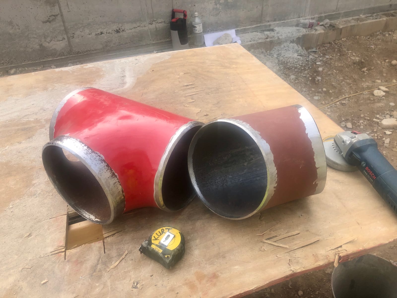 Red-coated fabricated tee and a bevelled pipe end on the site bench