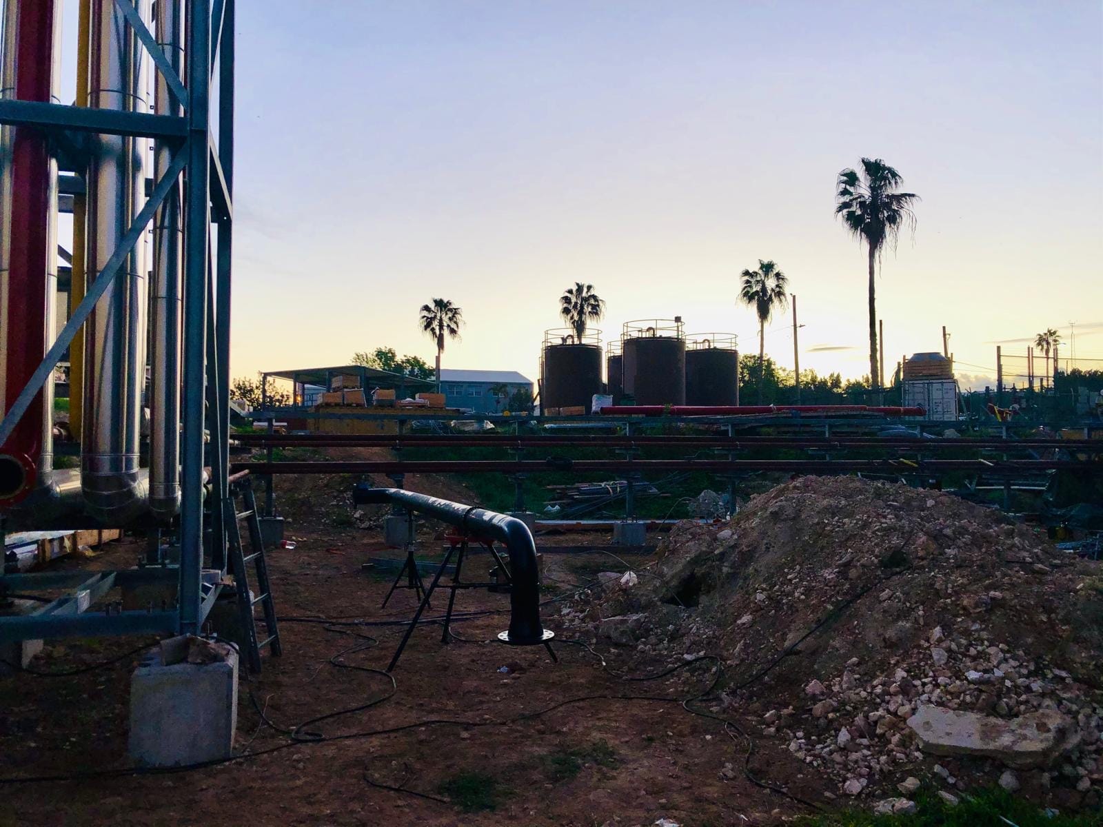 Black-coated fire main up on stands at dusk, with the plant and storage tanks behind