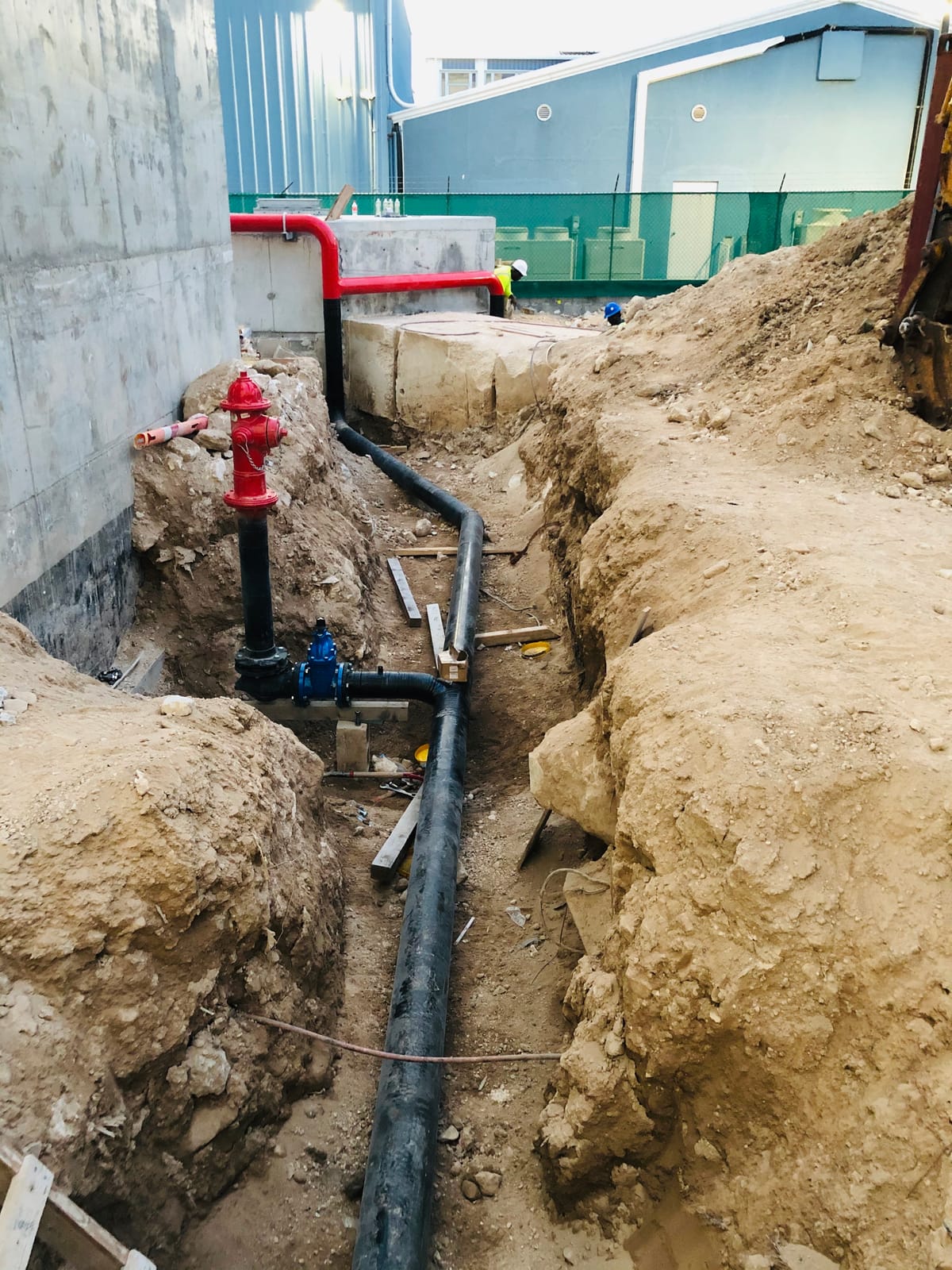 Red fire hydrant standing off the buried main, the black-coated pipe running away down the trench